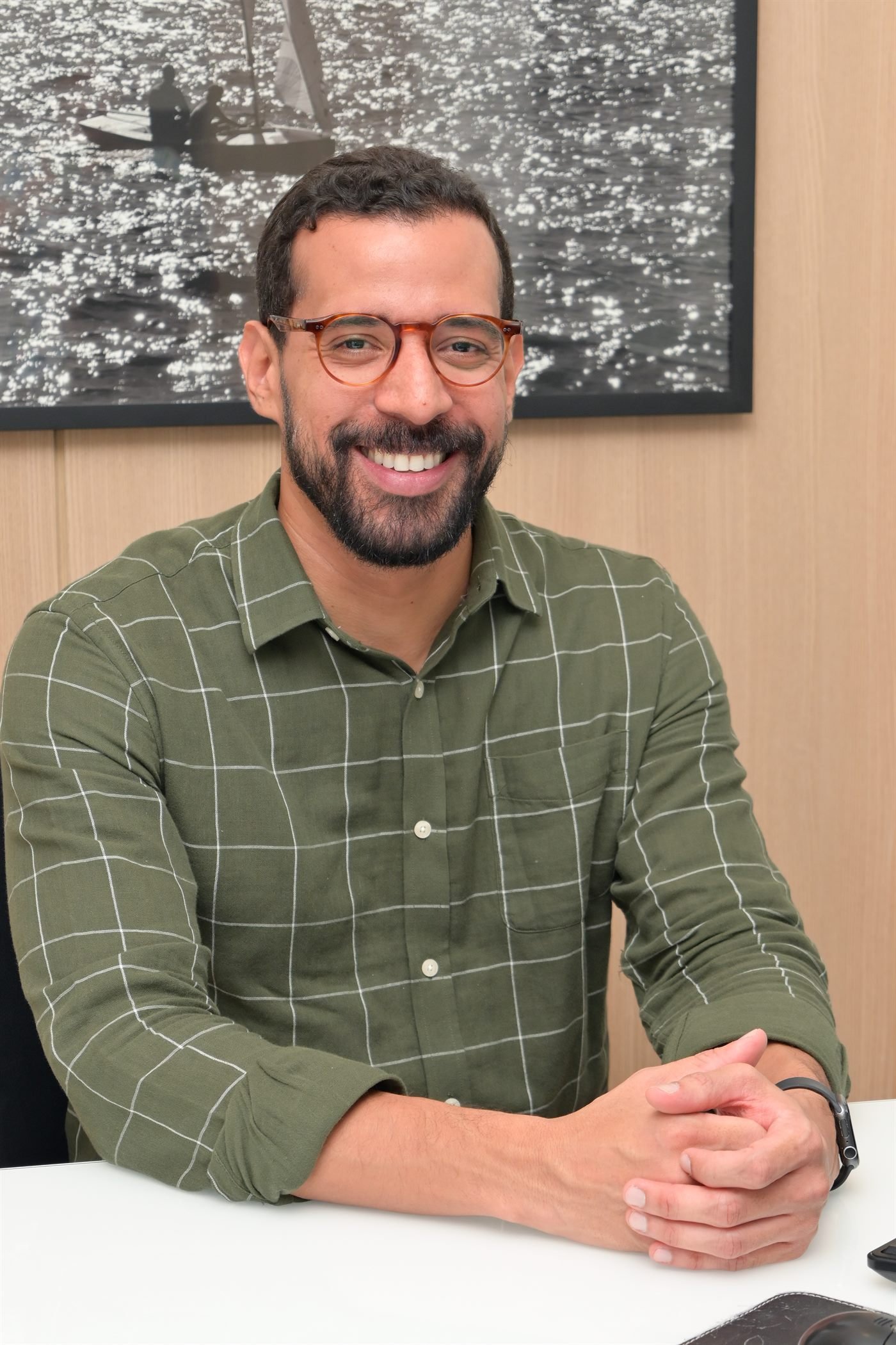 Dr. Uri Ramos de camisa verde, sorrindo, com as mãos entrelaçadas sobre a mesa do consultório